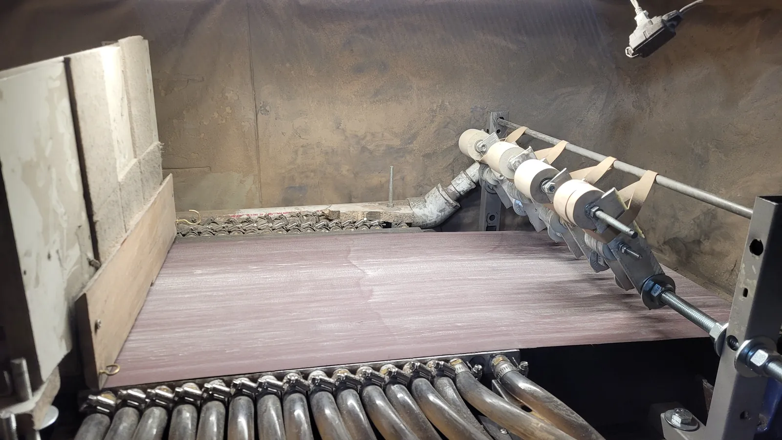 Sanding belt running over the cooled plate of the water-cooled sanding table, with water lines along the front and guide wheels on the right